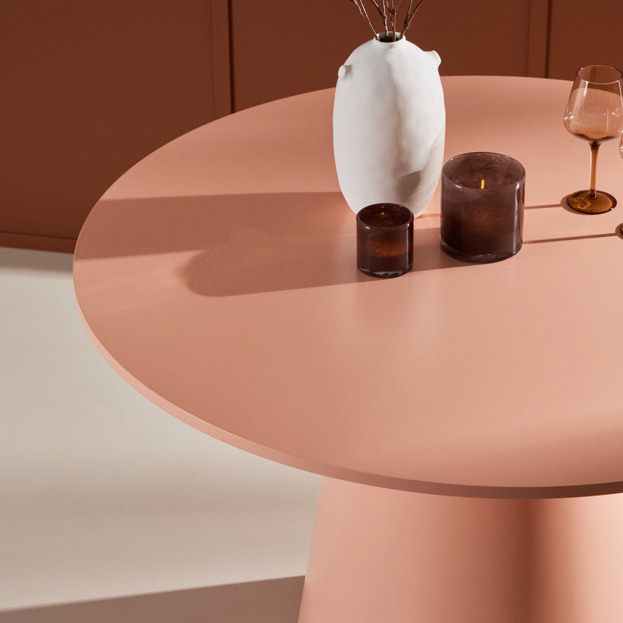 Venture Home Lanzo Matbord ⌀120 i Peach av Venture Home fungerar som en mittpunkt med en vit vas, två bärnstensfärgade glas och ett mörkt ljus. Den sticker ut mot en koordinerande varmtonad vägg i den minimalistiska, eleganta miljön.