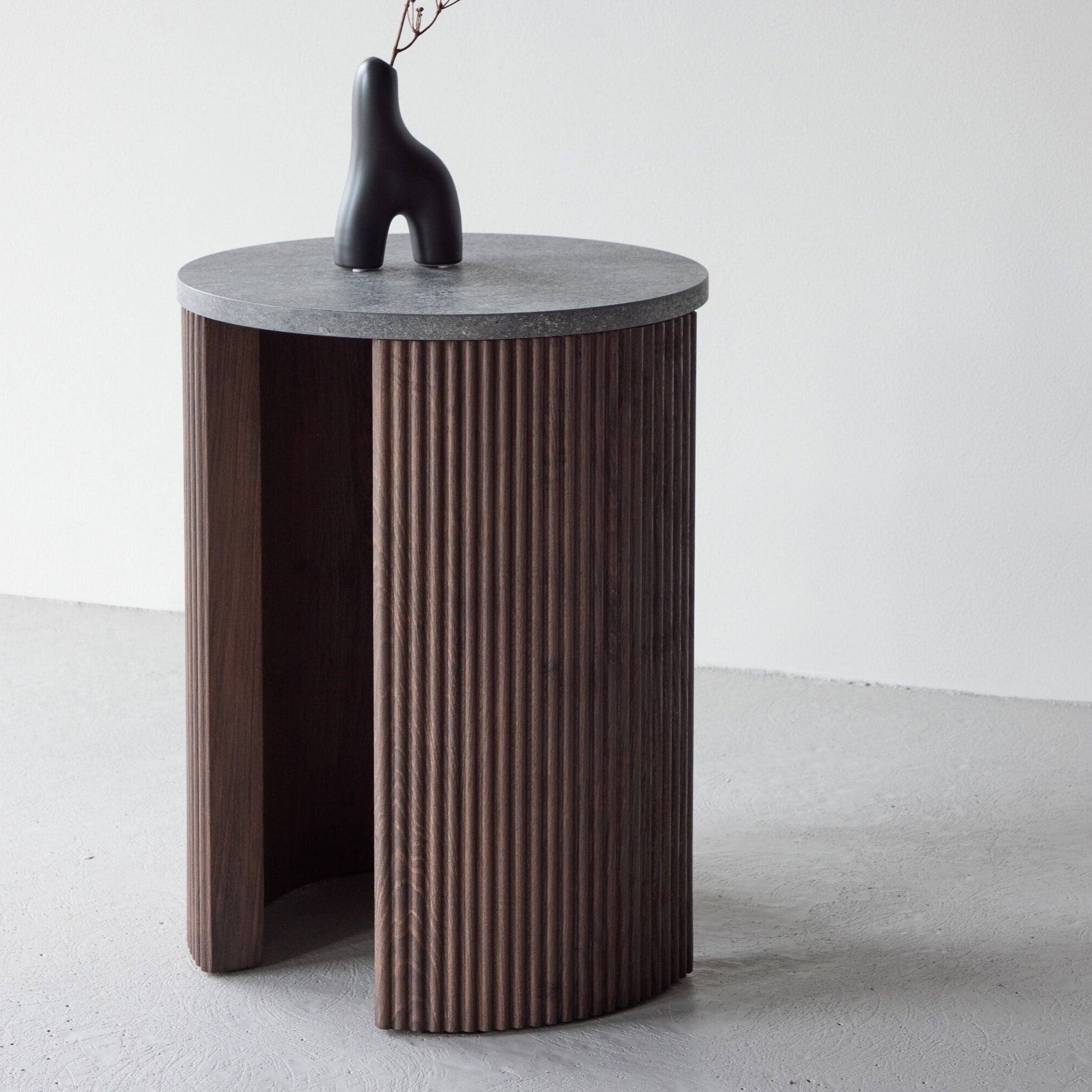 The Bristol Sidobord - Rund marmorlook i mocca från Venture Home har en marmorinspirerad bordsskiva och ribbad, välvd träbas. På bordet står en minimalistisk svart abstrakt vas med en enkel kvist.