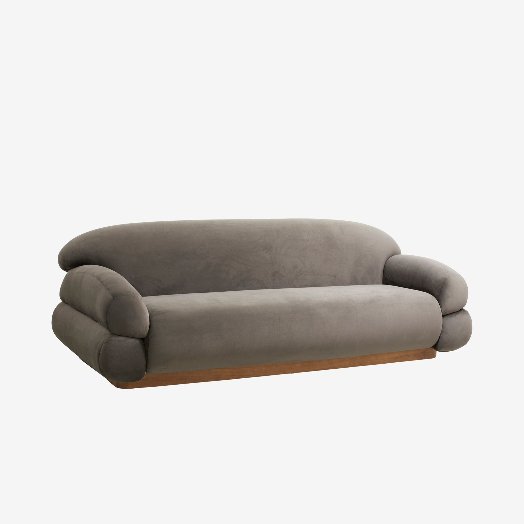 Soffa i varmgrå sammet med rundade, organiska former och låg träbas. Den har en skulptural och mjuk design med överdimensionerade arm- och ryggstöd som skapar en inbjudande loungestil. Perfekt för moderna och eleganta inredningar.