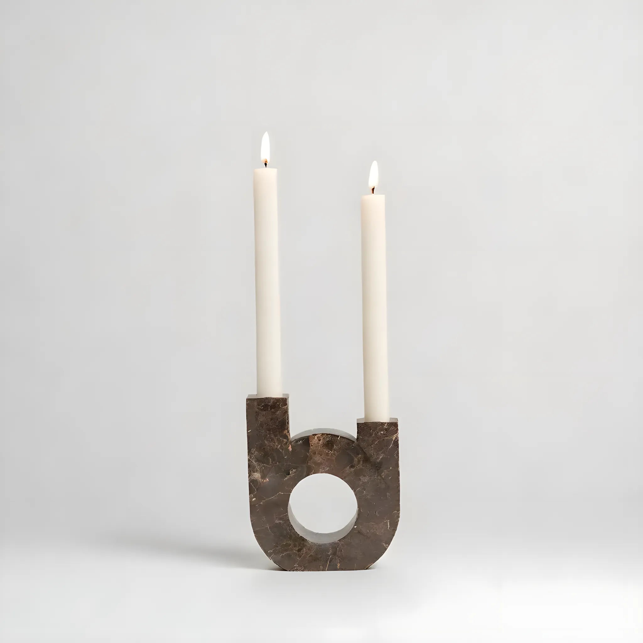 Modern ljusstake i marmor med två vita ljus, med en unik U-formad design och en polerad brun stenfinish.