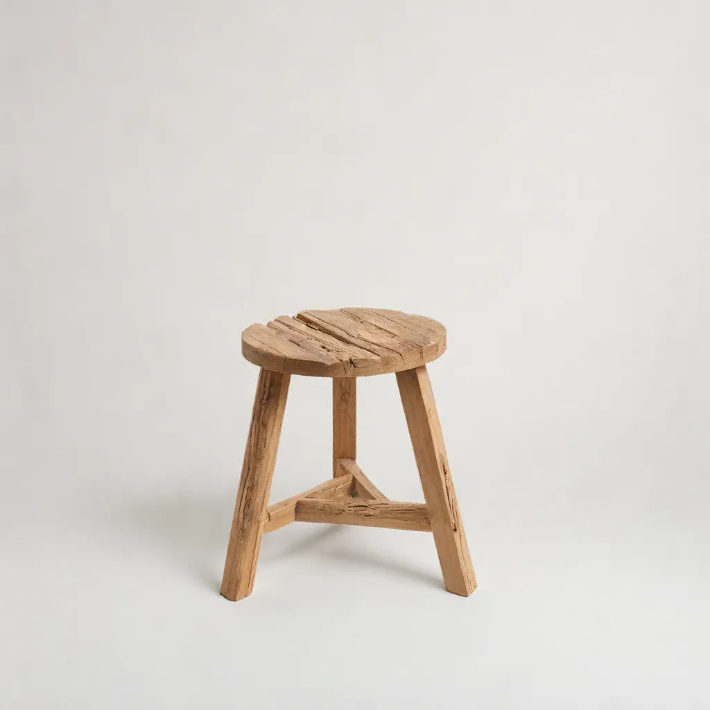 På en benvit bakgrund sitter Yatai Pall i Återvunnet Teakträ – Rustik Charm - L från bazar bizar, en rustik rund träpall med en enkel trebent design och naturlig träfinish, som visar upp sin ådring, struktur, eleganta detalj och rustik. charm.