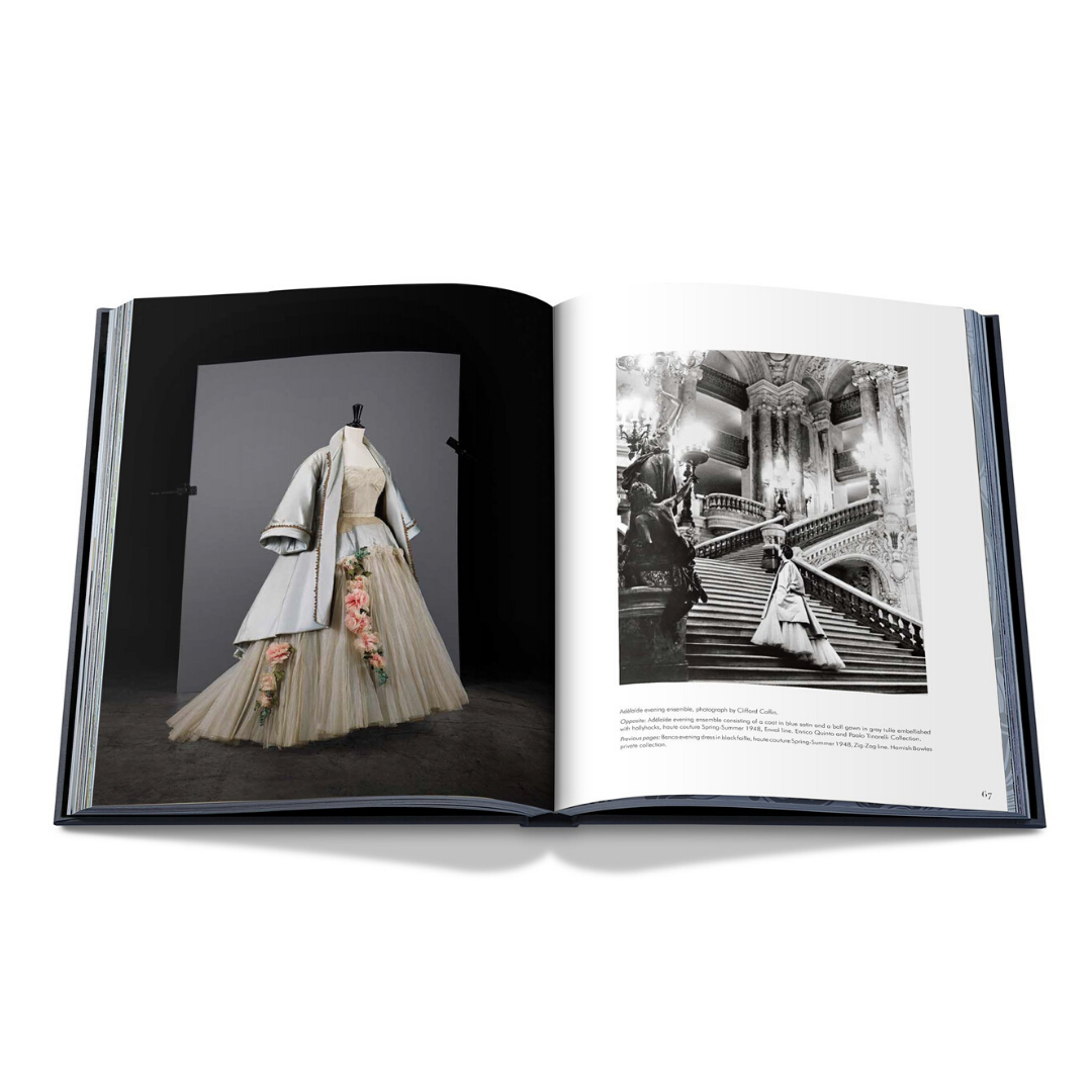En öppen bok visar upp ett tvåsidigt uppslag från "Dior av Christian Dior" av New Mags. Till vänster visar ett färgfoto en Dior-klänning med rosa blommiga accenter och en ljusblå kappa. Den högra sidan erbjuder en svart-vit bild av en kvinna som går ner för en utsmyckad trappa på liknande haute couture-sätt.