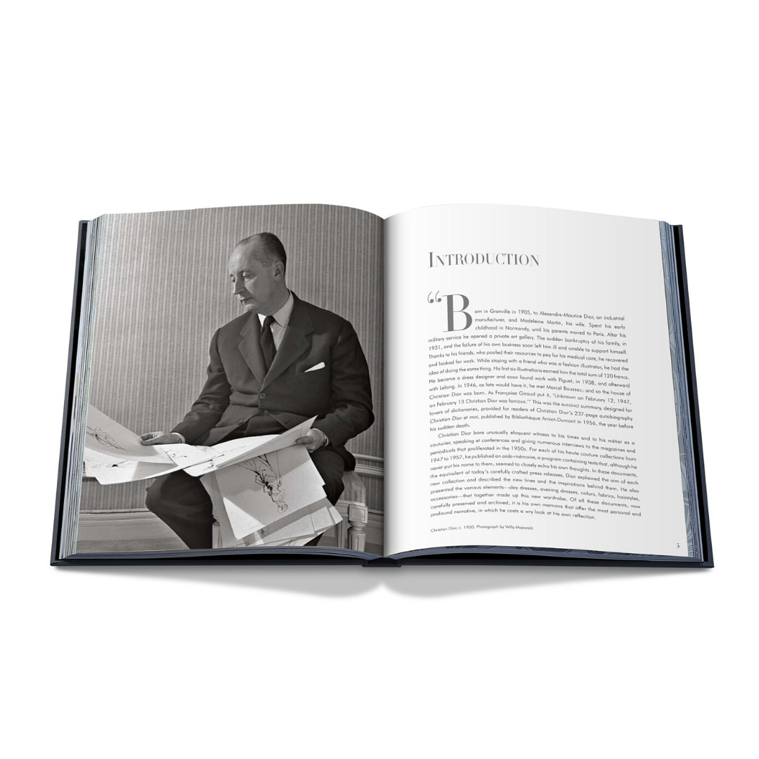 Boken "Dior av Christian Dior" från New Mags öppnar för ett svartvitt foto av en man som studerar papper på vänster sida. På den högra sidan visas ordet "Introduktion" med en stilren lock "B" och flera stycken, elegant vilande på en vit yta.