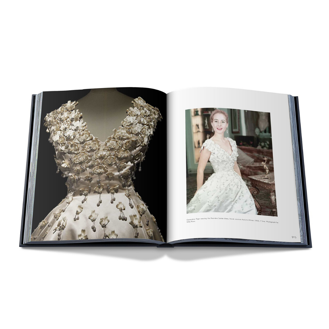 På vänster sida visar en öppen bok en närbild av en vit haute couture-klänning med blommiga applikationer. Den högra sidan visar en kvinna som bär en liknande designad blommig klänning, som utstrålar den tidlösa elegansen av "Dior by Christian Dior", publicerad av New Mags.