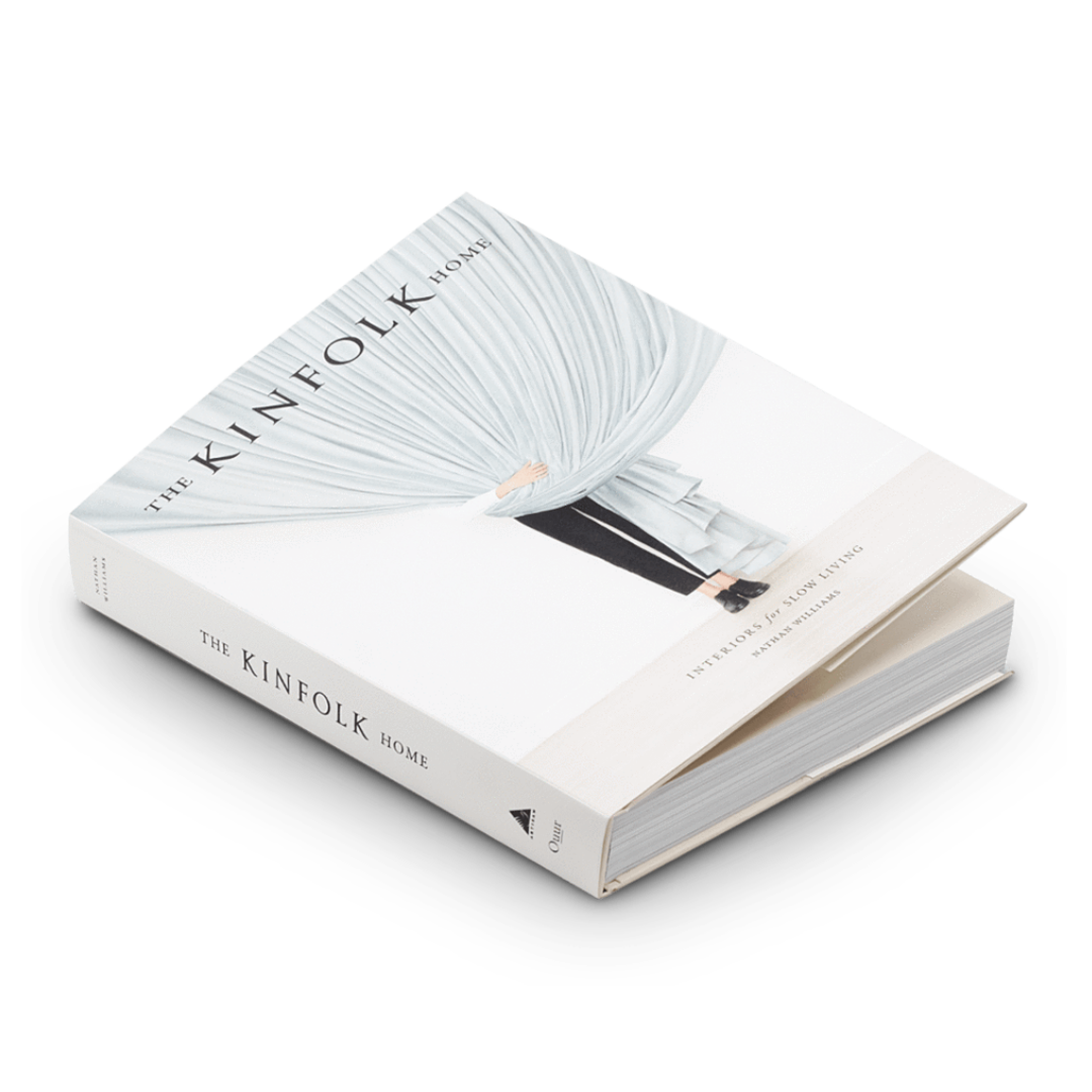 Den inbundna "The Kinfolk Home" av New Mags visar upp sin minimalistiska design med ett omslagsfoto av någon som håller ett stort vitt draperat tyg. Dess ryggrad visar titeln, inbjuder till en djupgående utforskning av design och fångar essensen av inredningsintresse.