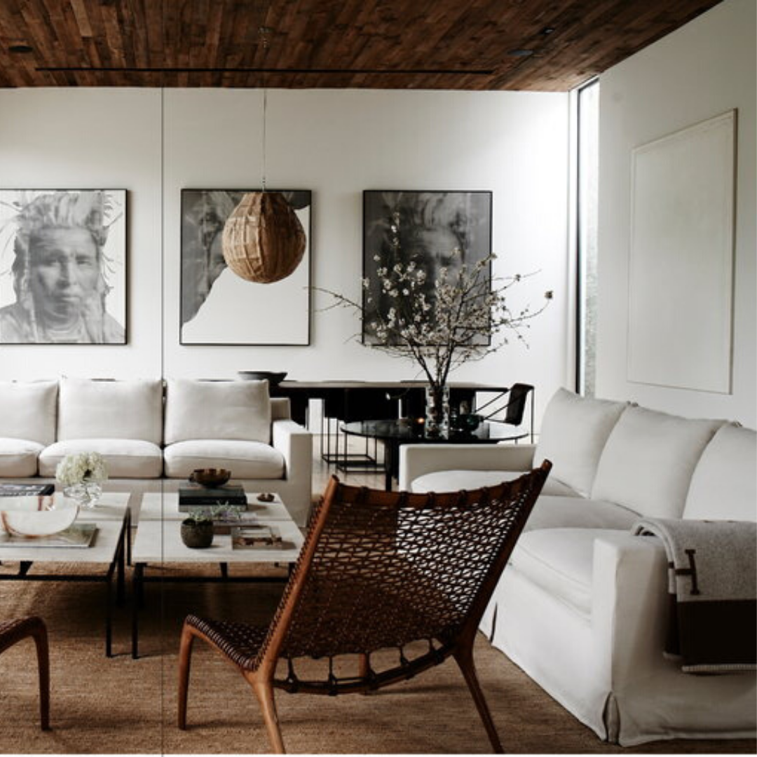 Inspirerat av New Mags' Kinfolk Home-estetik, har detta eleganta vardagsrum ett trätak och neutrala toner. Den har vita soffor, en vävd stol och ett soffbord i glas med böcker. Abstrakt väggkonst kompletterar utrymmet, medan blommiga grenar i en vas ger liv under en sfärisk taklampa.