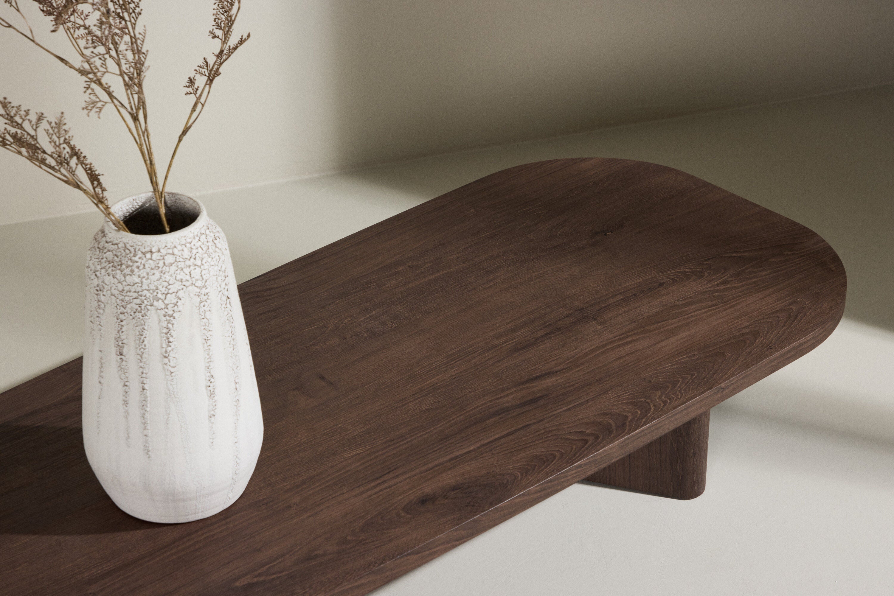 En stor vit keramikvas med torkade grenar vilar på Grönvik Soffbord – Avlångt soffbord i mocca från Venture Home, mot en ljus neutral bakgrund för en minimalistisk och modern look.