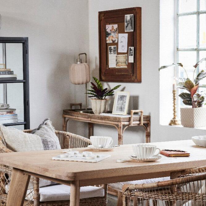 En matsal med korgstolar runt ett bord, kompletterad med en lampa med en beige skärm mot en vit bakgrund.