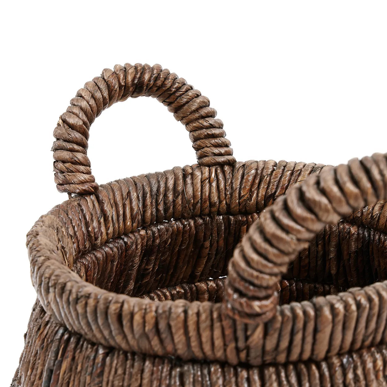 Närbild av en rund vävd korg gjord av bruna naturfibrer. Chisomo Handflätad Korg i Bananblad från bazar bizar har två tjocka, robusta handtag, också gjorda av samma vävda material. Strukturen antyder en rustik, handgjord kvalitet. Korgen verkar vara tom.