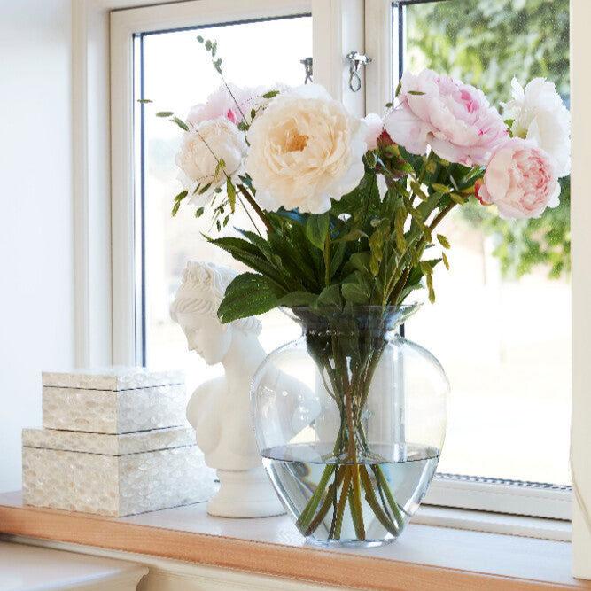 En vas fylld med rosa och vita blommor vilar på en solig fönsterbräda och ger rummet en touch av skönhet.