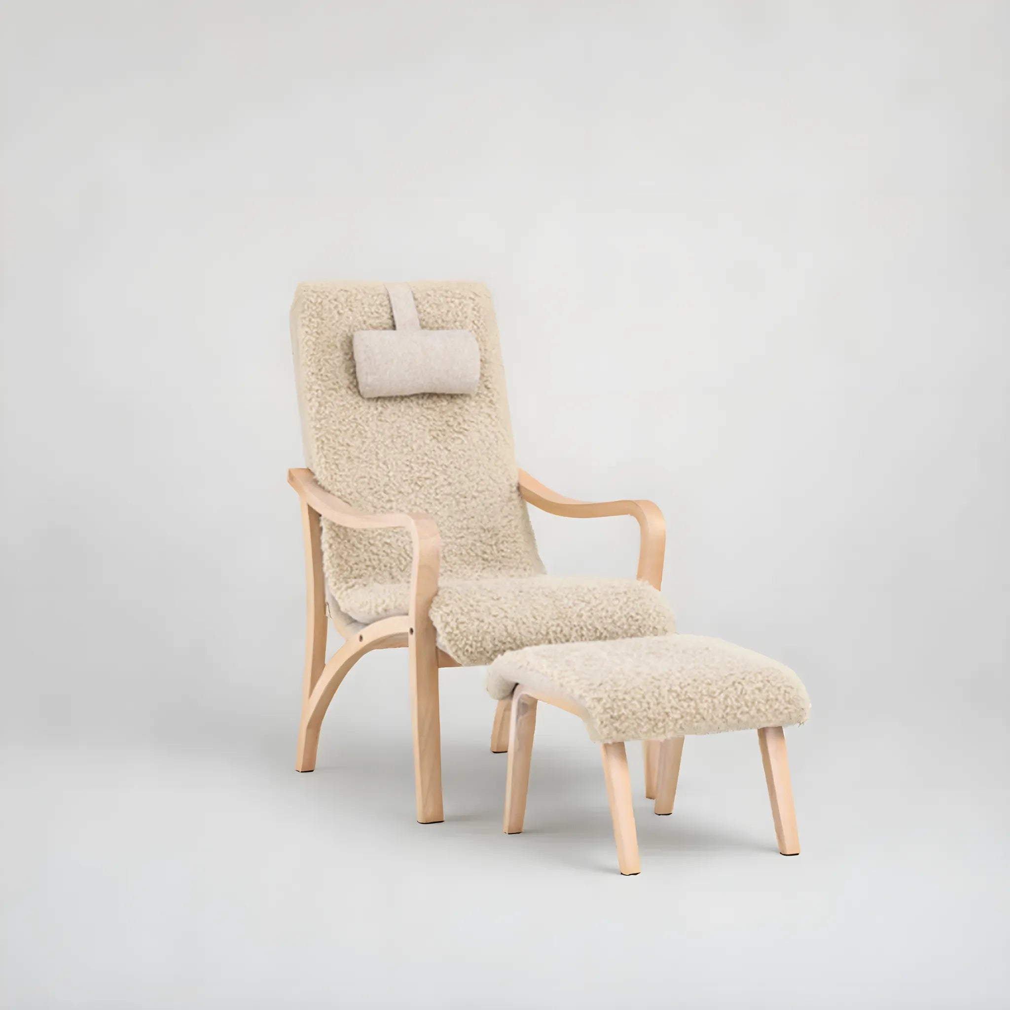 Fårö fåtölj med fotpall och nackkudde från Venture Home har en ljus träram med pälsliknande polyestertyg, böjda armstöd och en rektangulär huvudkudde, som visar upp sin skandinaviska design och komfort på en blekgrå bakgrund.