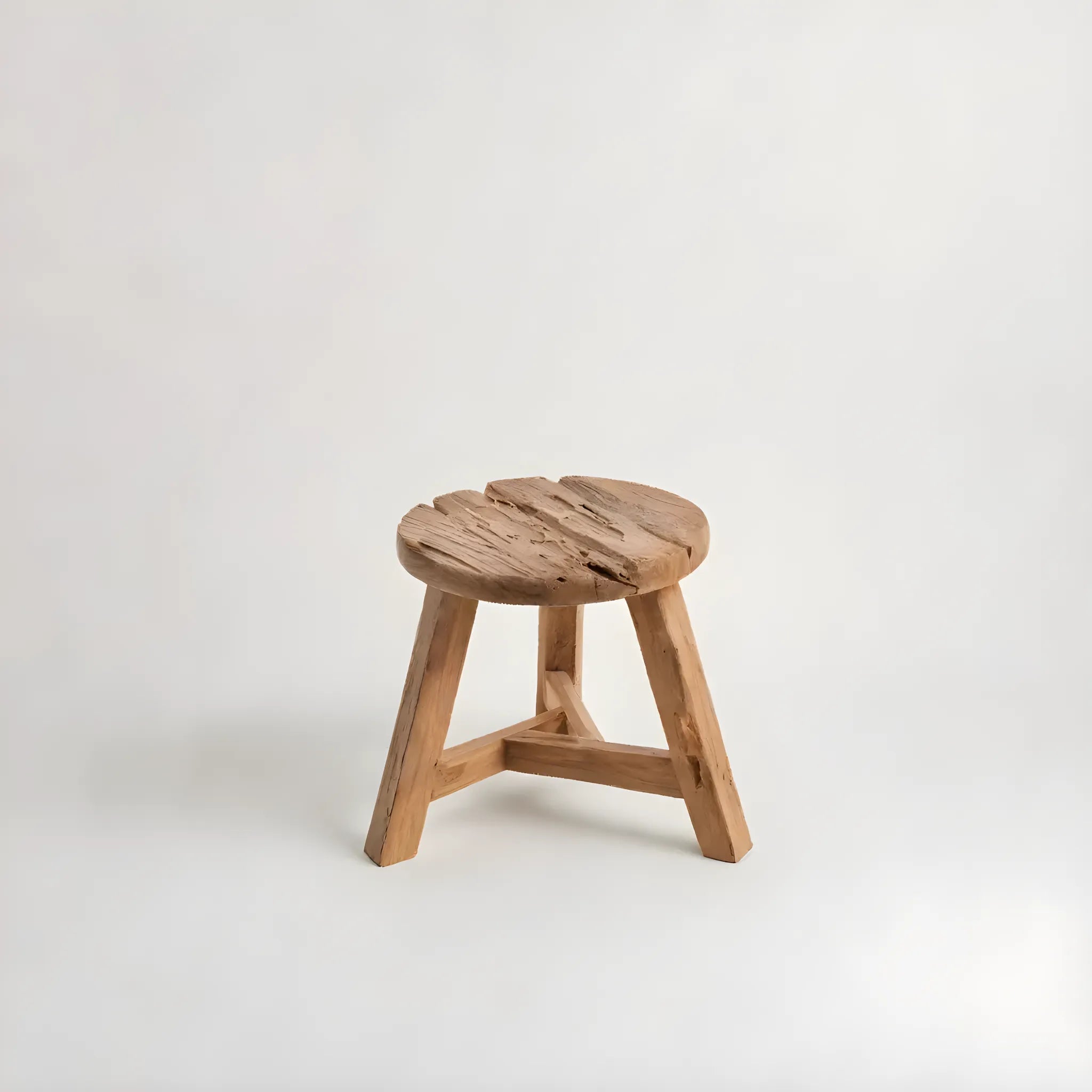 Yatai Pall i Återvunnet Teakträ – M av bazar bizar är en enkel träpall med en rund topp och tre ben, mot en vanlig vit bakgrund. Tillverkad av återvunnen teak, har den en naturlig, oavslutad look med synliga träfibrer och rustik färg.