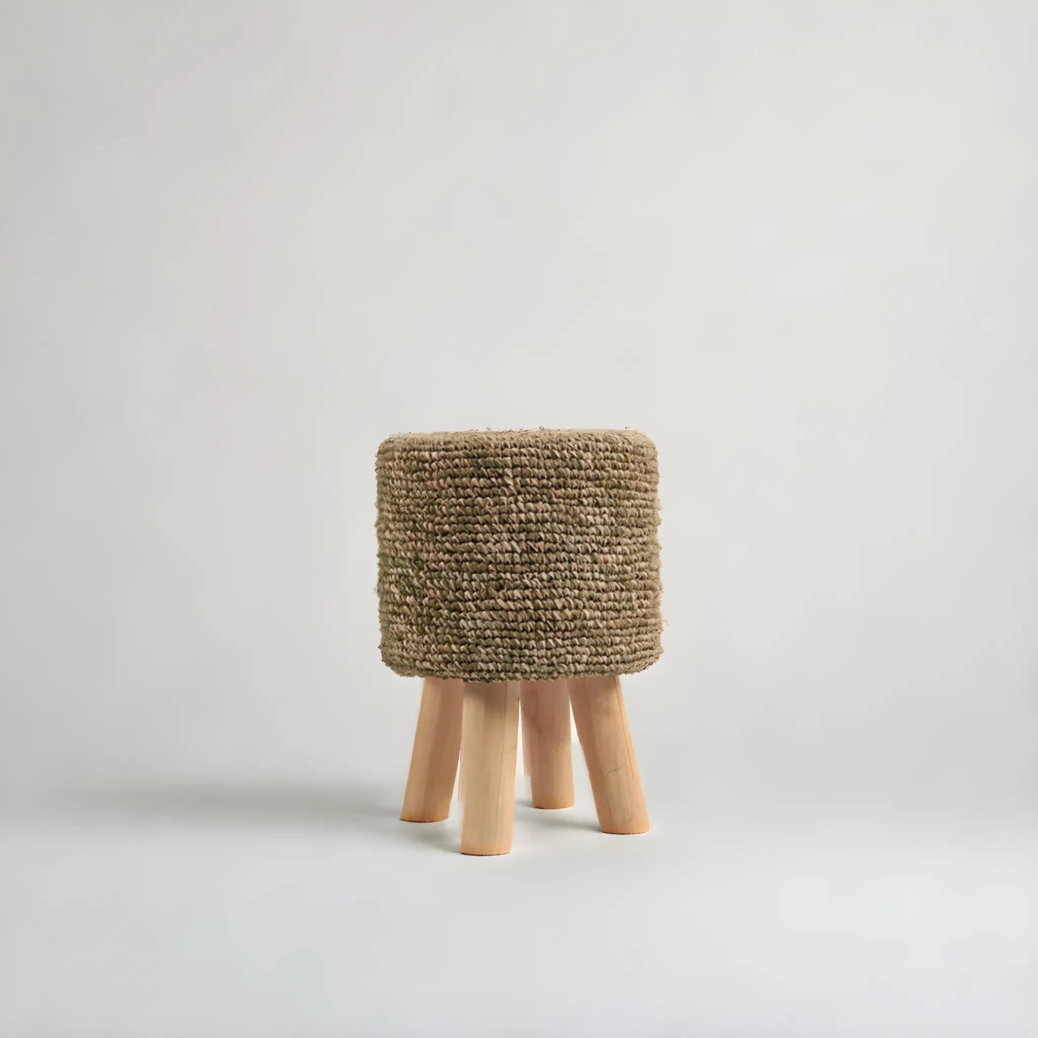 Raffia Tressed Pall från bazar bizar är en liten, rund pall med en strukturerad beige raffiasits och fyra ljusa träben – en miljövänlig inredningsdetalj mot en vanlig vit bakgrund.